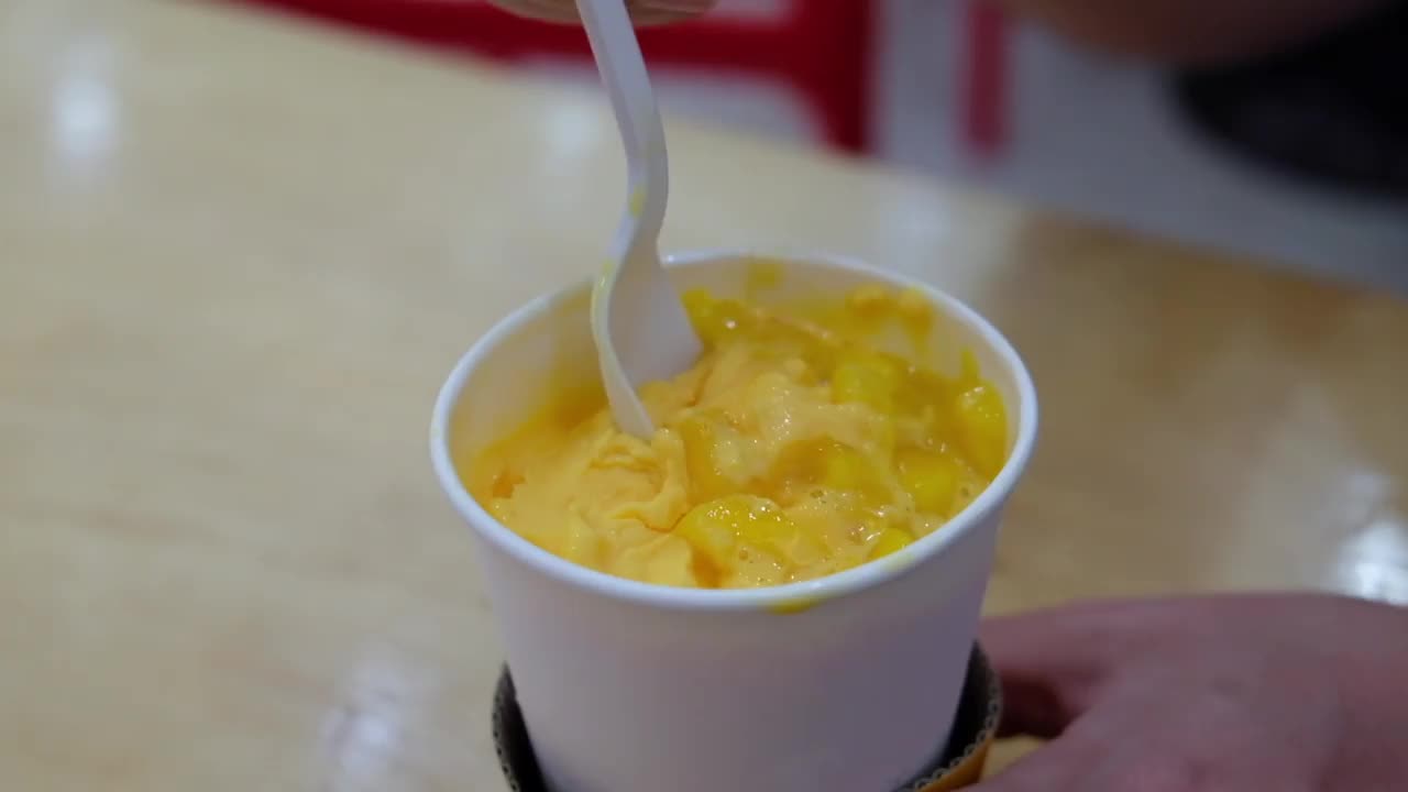 一个男人手里拿着一个白色的勺子，从一个白色的杯子里拿起黄色的芒果片冰淇淋视频下载