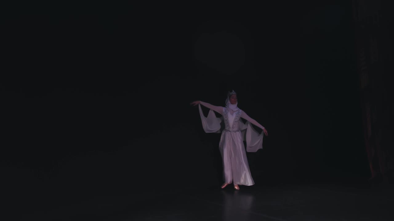 芭蕾舞演员走上舞台。一位芭蕾舞演员穿着美丽的白色长袍在黑色背景上跳舞。Raymonda变异。视频素材