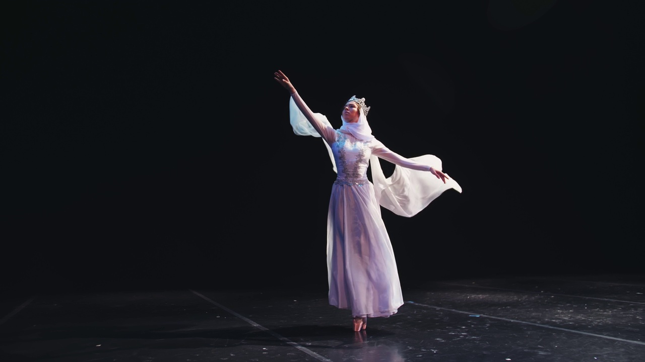 一位芭蕾舞女演员穿着漂亮的白色套装，头戴皇冠，美丽地站在剧院的舞台上。风吹着她的衣服。自由的概念，决心。视频素材