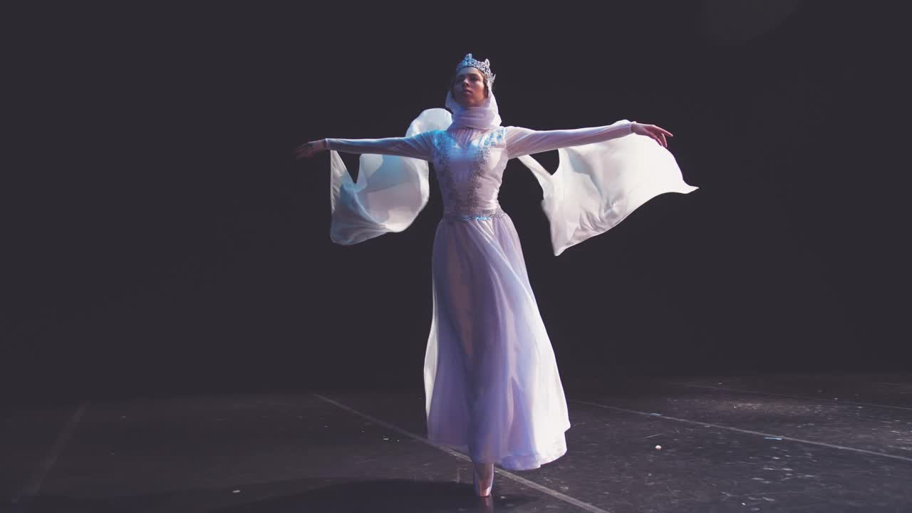 一位优雅、勤劳的芭蕾舞女演员头戴皇冠，在黑色背景上摆出美丽的姿势。风吹着她美丽的白色套装。雷蒙达的变奏曲。《泰坦尼克号》。视频素材
