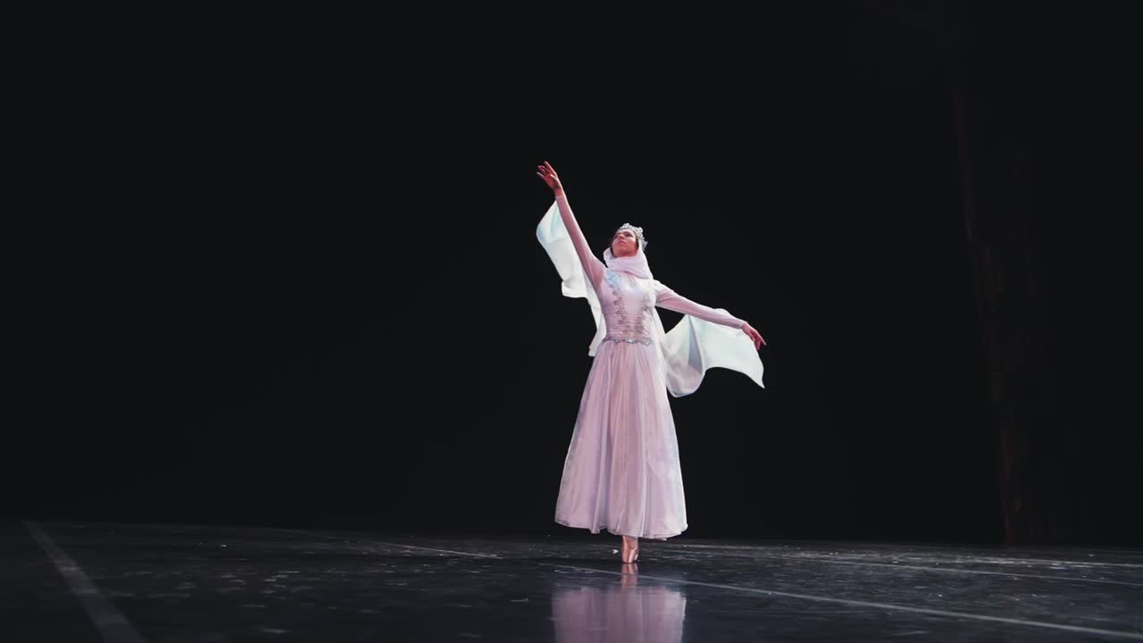 一位优雅、勤奋的芭蕾舞演员在黑色背景上表演美丽的芭蕾元素。风吹着她美丽的白色套装。缓慢的运动。视频素材