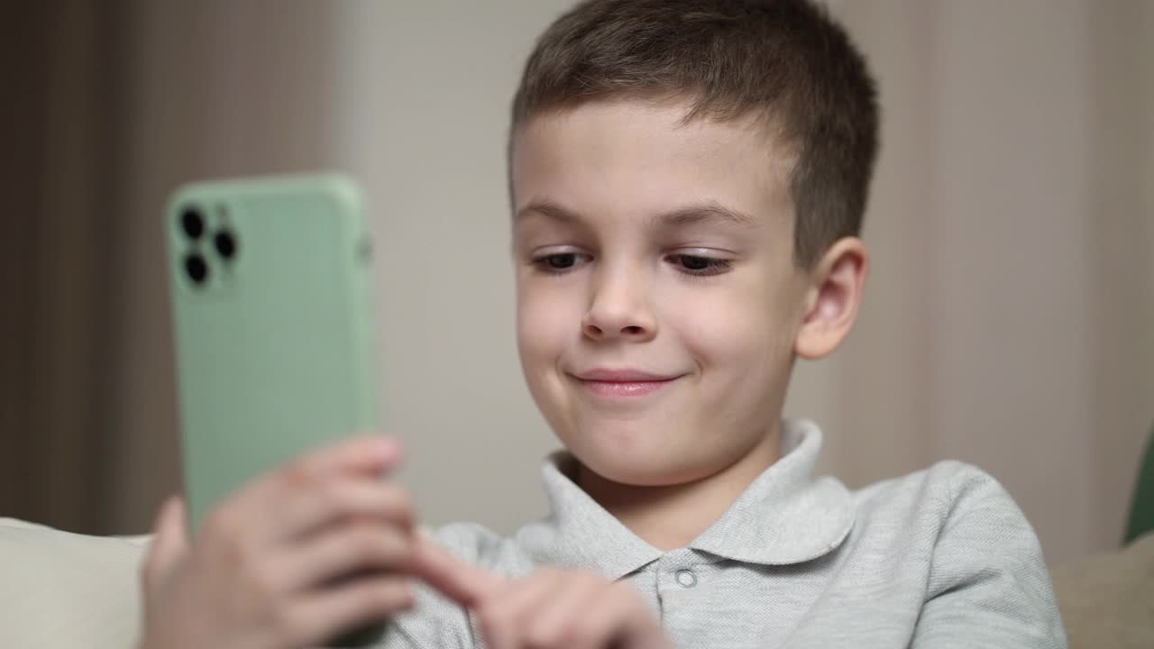 一个七岁的男孩坐在家里的沙发上，把空闲时间都花在手机上，看社交网络上的热门内容。视频下载