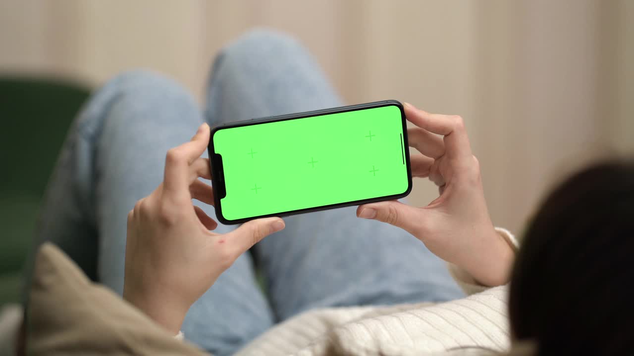 女人躺在沙发上休息，使用绿屏和色度键的手机。视频下载