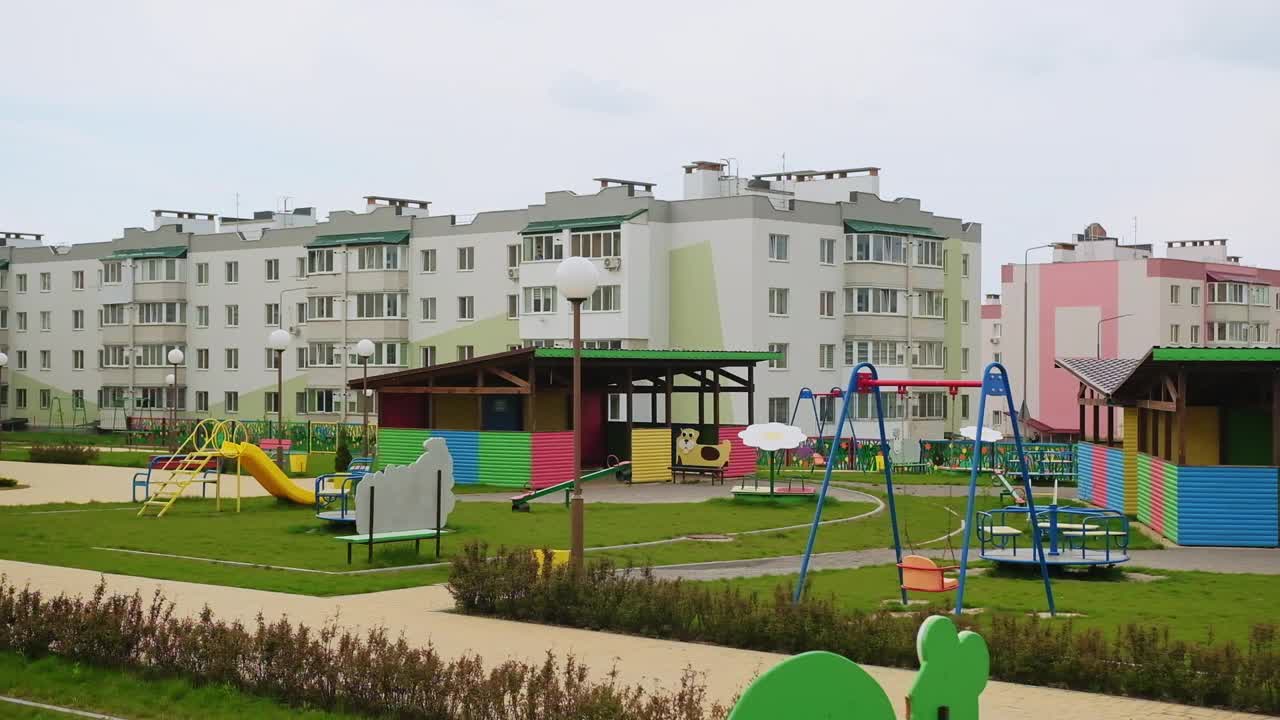 新建幼儿园守得好好的地盘。绿色草坪上的大凉亭和跷跷板，背景是新房子。视频素材
