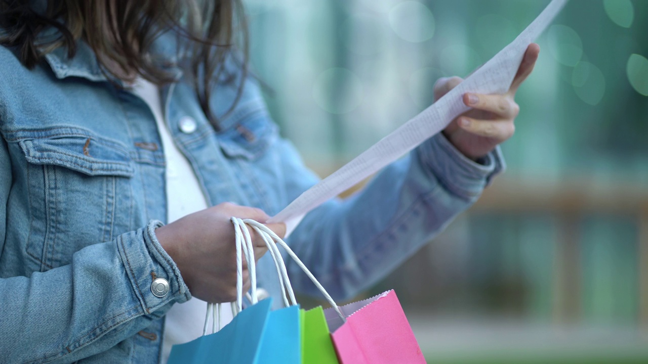 一位女士站在购物中心附近，拿着现金收据和纸袋分析商品价格的特写。视频下载