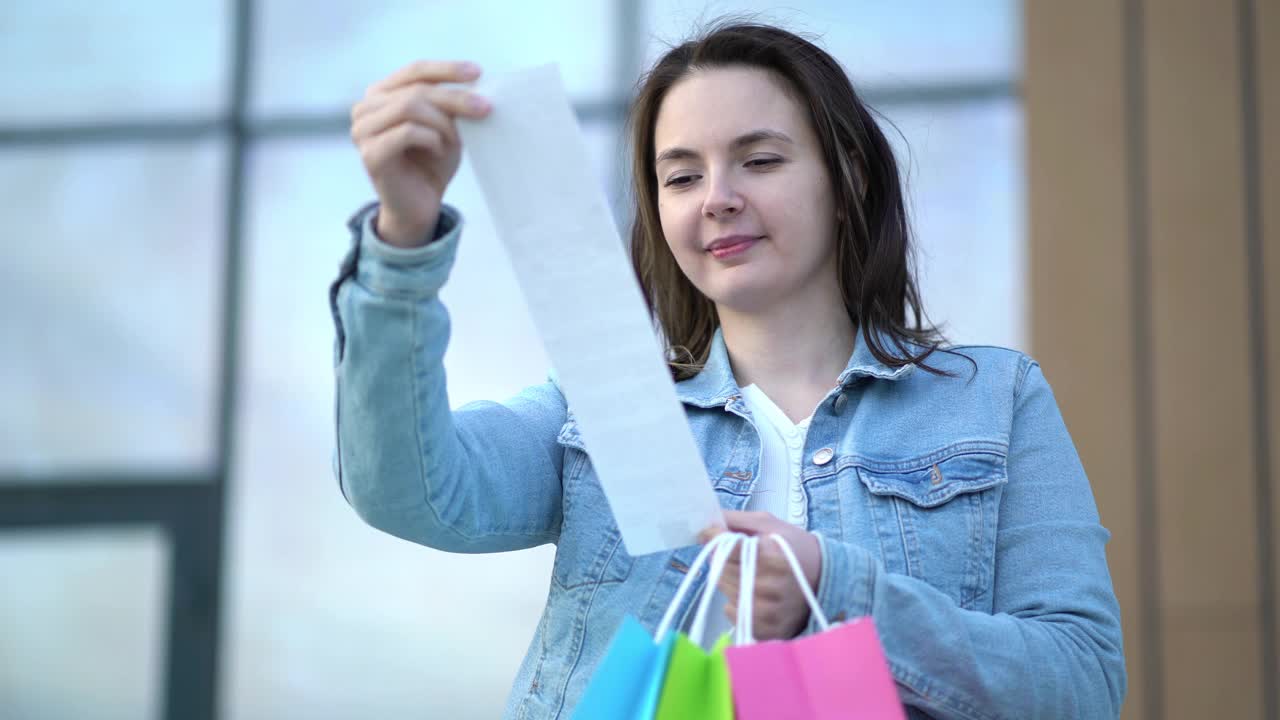 在购物中心购物后，年轻女子看着现金收据上商品的价格视频下载