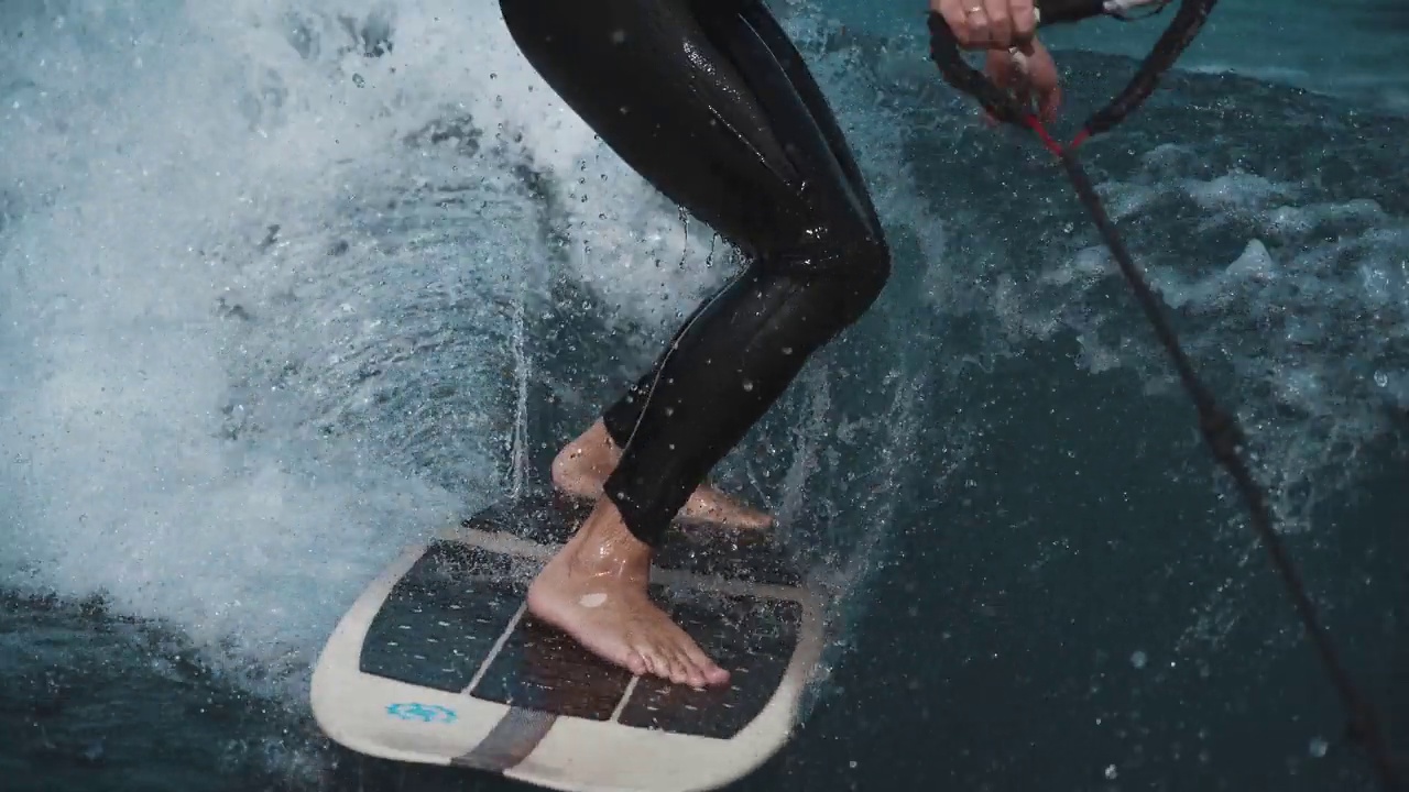 Wakesurfing。一个男子腿的冲浪板特写。穿着潜水服冲浪。特技，水上骑行。水上运动。夏天，色彩鲜艳。4 k视频下载