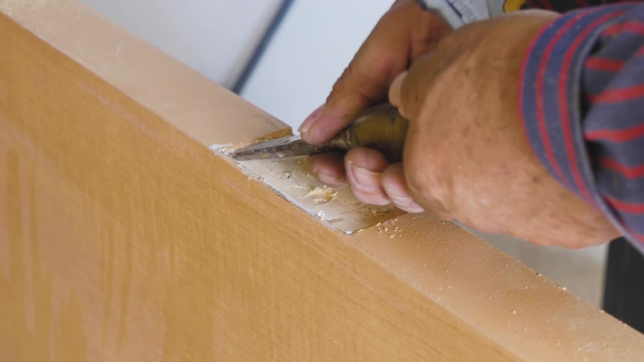 一名男性建筑工人正在用手凿开一扇门，以便门铰链能牢固地贴合。木门合页安装的近距离木匠工艺。门铰链安装。铰链和总成。视频下载