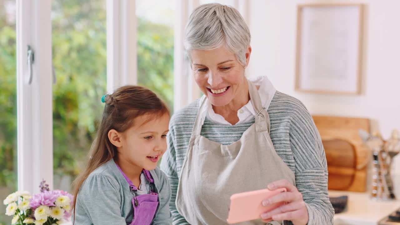 家庭，电话和祖母与女孩视频通话，一起享受高质量的时间，周末和假期。烘焙后在厨房用智能手机和奶奶交流，爱和小孩视频素材