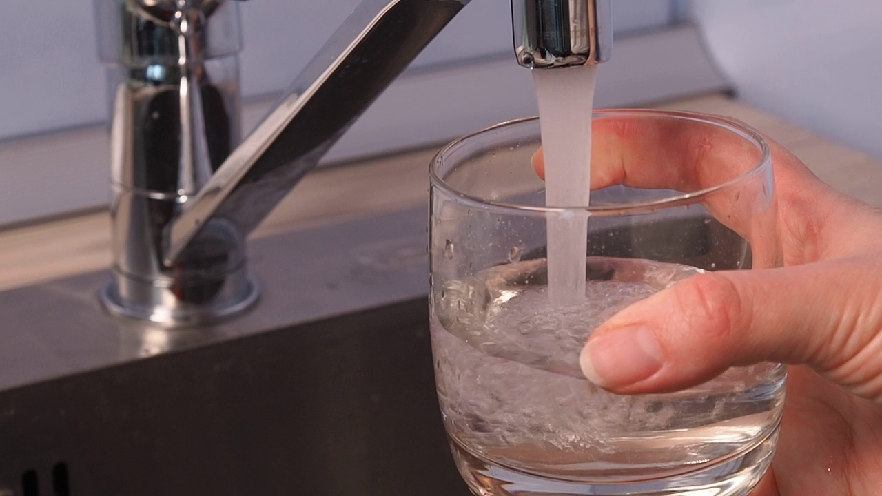 水正从厨房水槽里的水龙头里流出来。玻璃烧杯里装满了水。视频素材