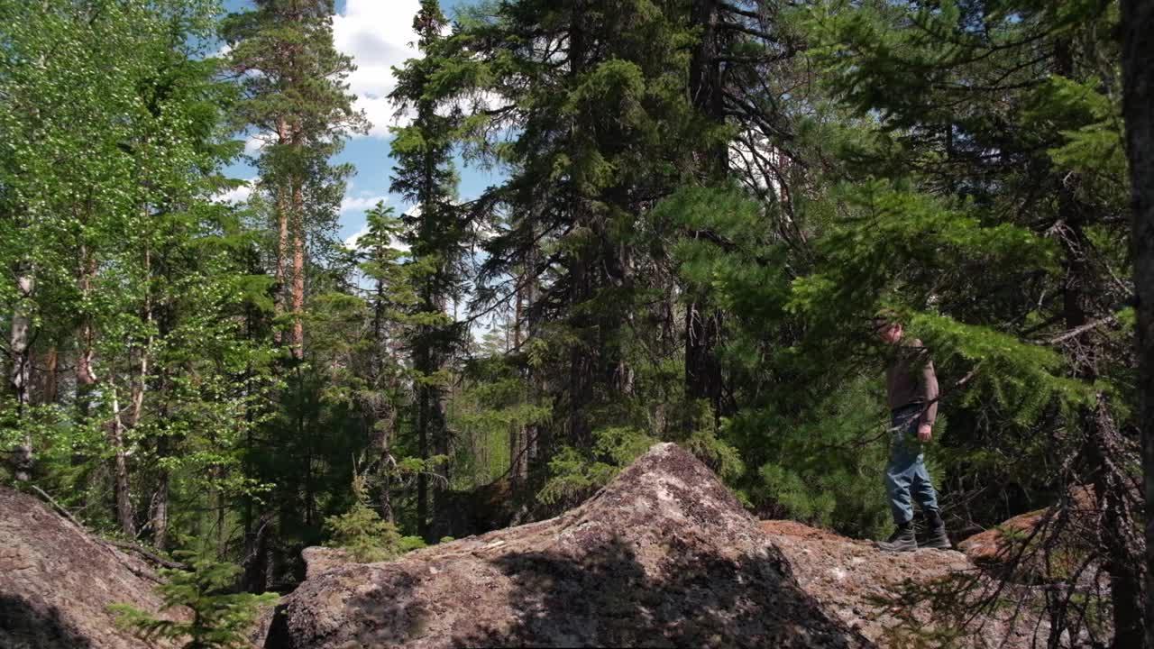 夏天，游客们在浓密的森林灌木丛中沿着高高的石头前行。缓慢的运动。视频素材