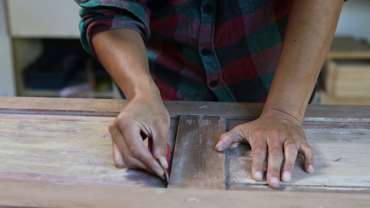 一位拉丁木工妇女正在用砂纸打磨一扇旧的木柜门，以修复它，在她的家庭作坊里。视频下载