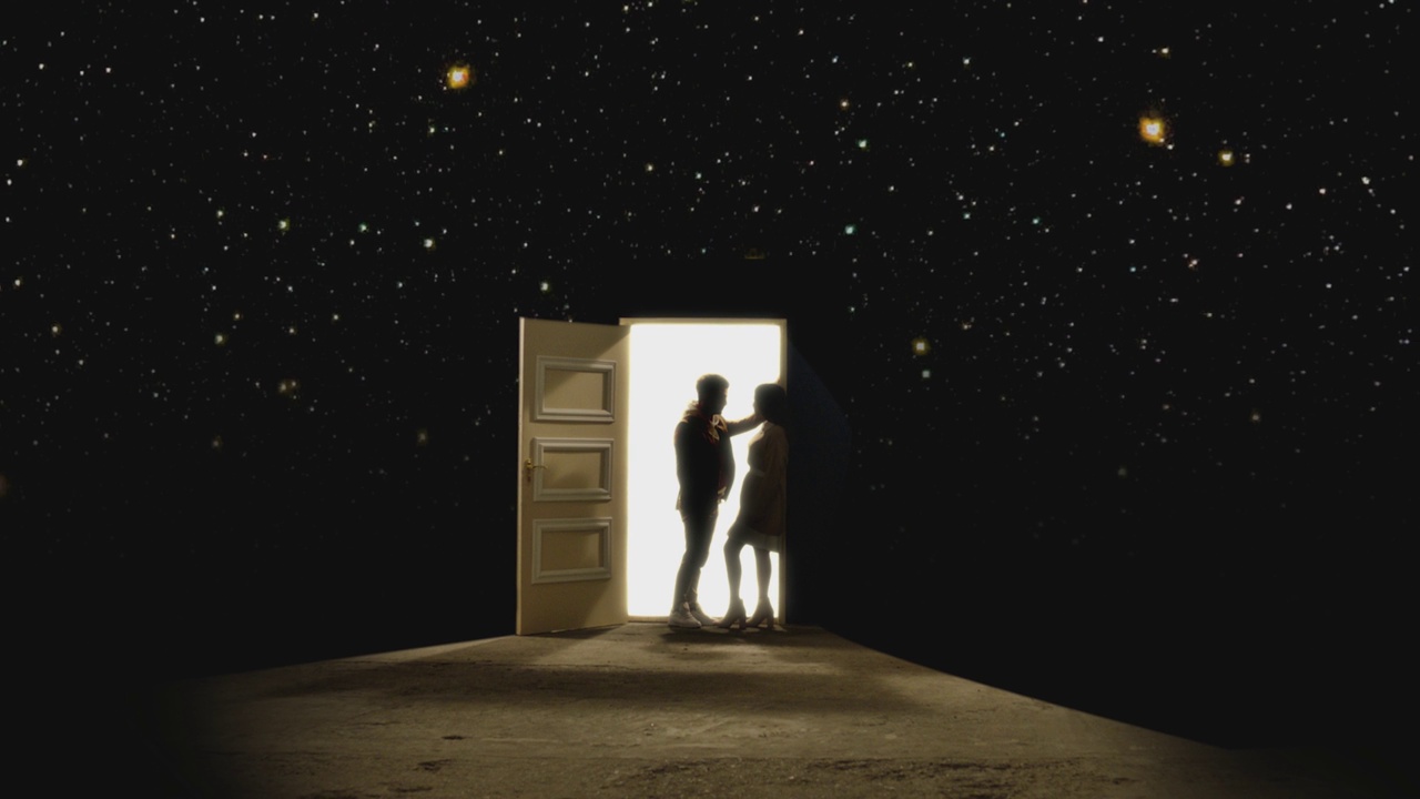 侧视图，一对夫妇对面站着，在一扇敞开的门前看着对方，后面有白色的光。一对情侣站在星星后面的地板上。梦想或浪漫的概念。慢动作视频素材