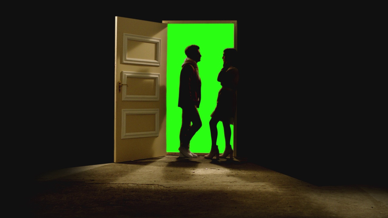 侧视图的夫妇站在对面，看着对方在一扇敞开的门后面的黑暗。镜头中，一对夫妇站在带有绿色屏风的门附近的地板上。梦想或浪漫的概念视频素材