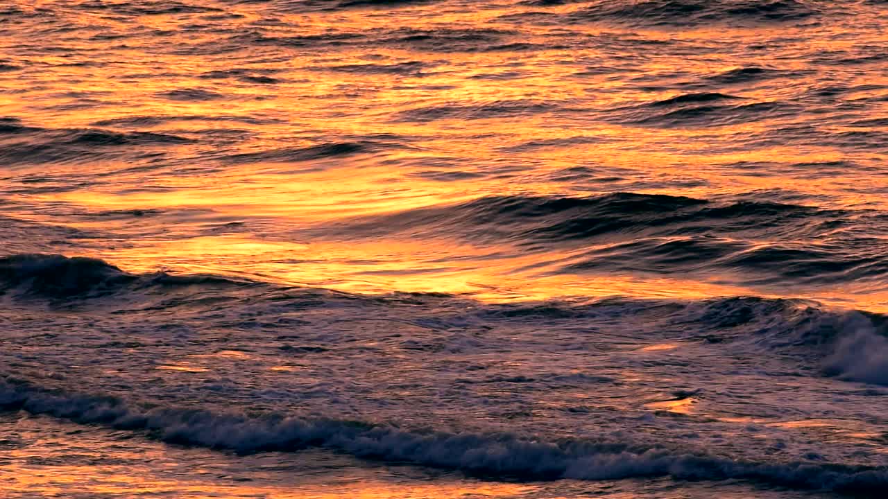 落日的海浪用橘黄色的阳光反射在沙滩上，近景，慢镜头。视频素材