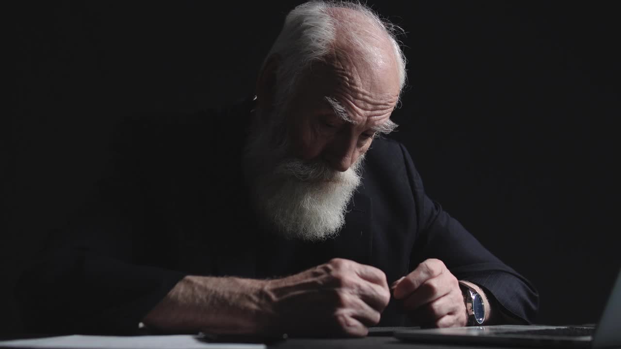 悲伤的老商人，灰色的胡子坐在办公桌旁，经济危机视频下载