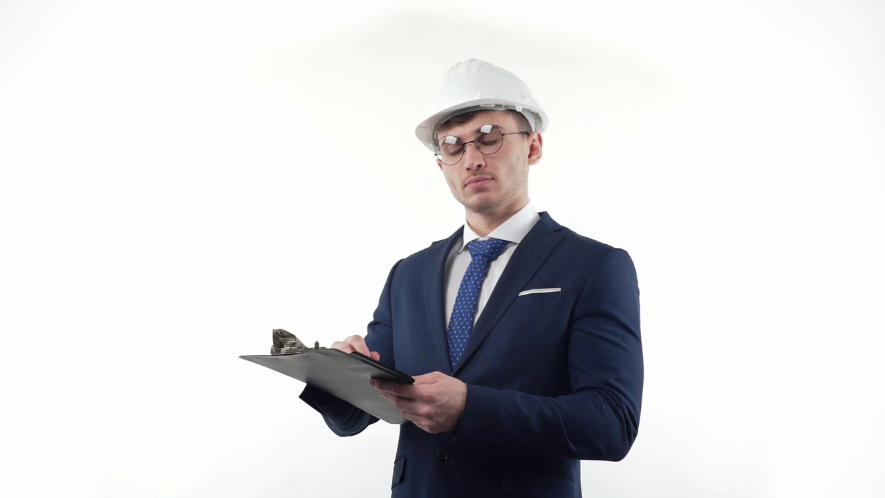 一名西装革履、戴着眼镜、戴着头盔的男商人一边思考，一边在笔记本上用笔做计划笔记。在白色的背景上。视频下载