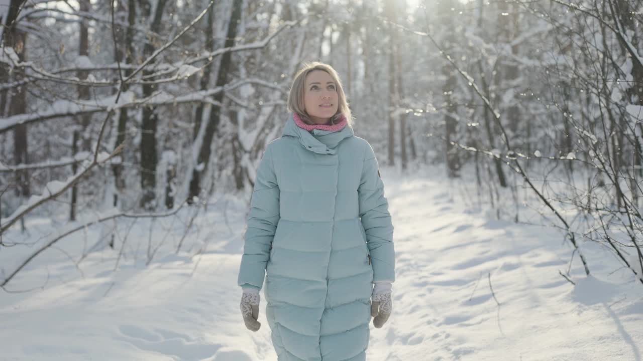 冬天，一个金发女人走过一片阳光明媚的白雪森林。享受自然视频素材