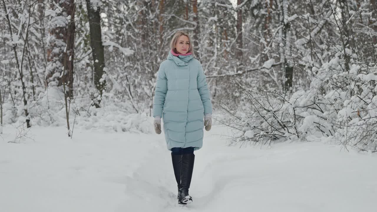 一个金发女人在冬天穿过白雪覆盖的森林视频素材