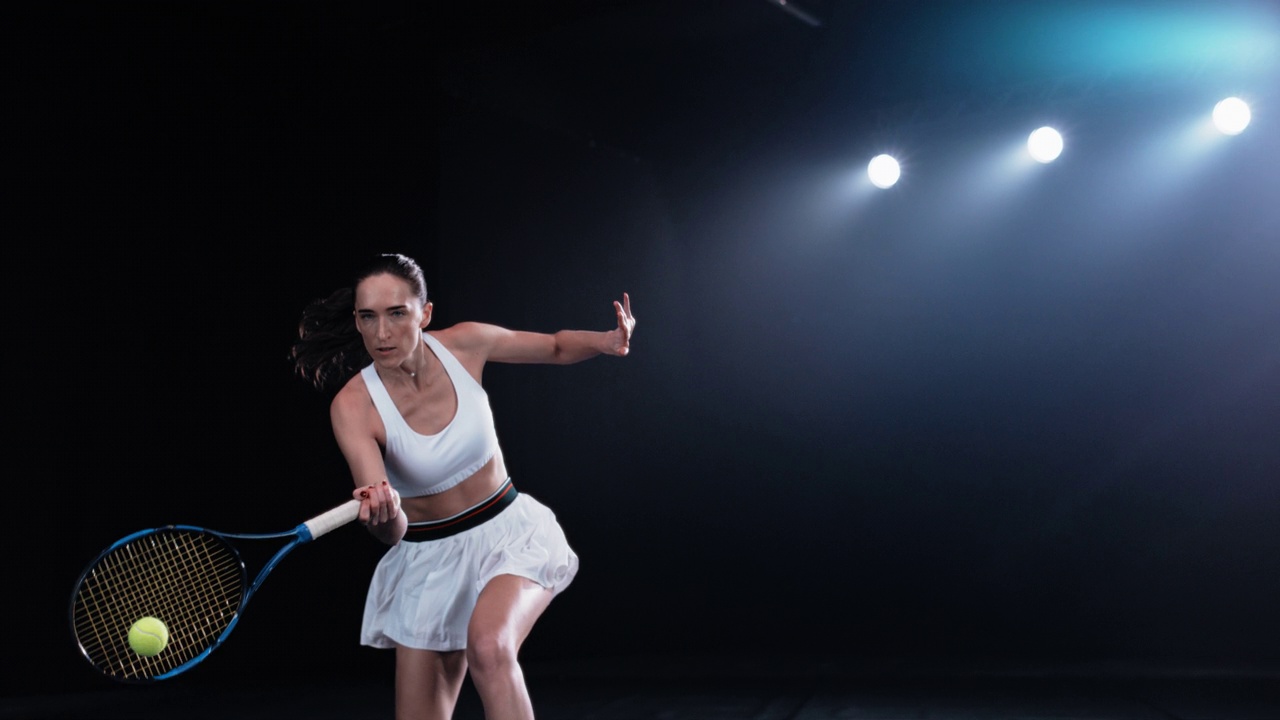 运动女网球运动员在黑色背景下在聚光灯下打低球的美学镜头。电影超级慢镜头捕捉了一个在锦标赛中获胜的强有力的正手击球视频下载