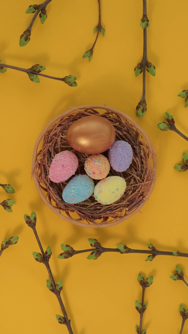 鹌鹑彩蛋在篮子里，黄色背景上旋转着绿色叶子的小树枝。复活节快乐垂直视频视频素材