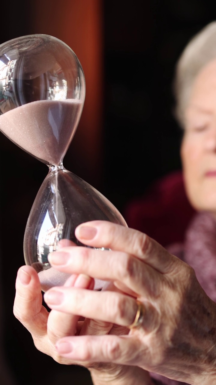 一个老妇人拿着沙漏的手。倒计时和时间的概念。视频下载