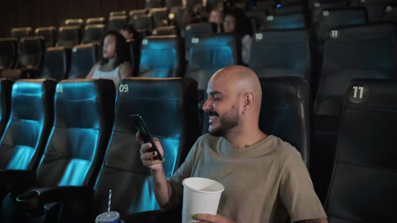 年轻人在电影院开始看电影前发短信视频素材