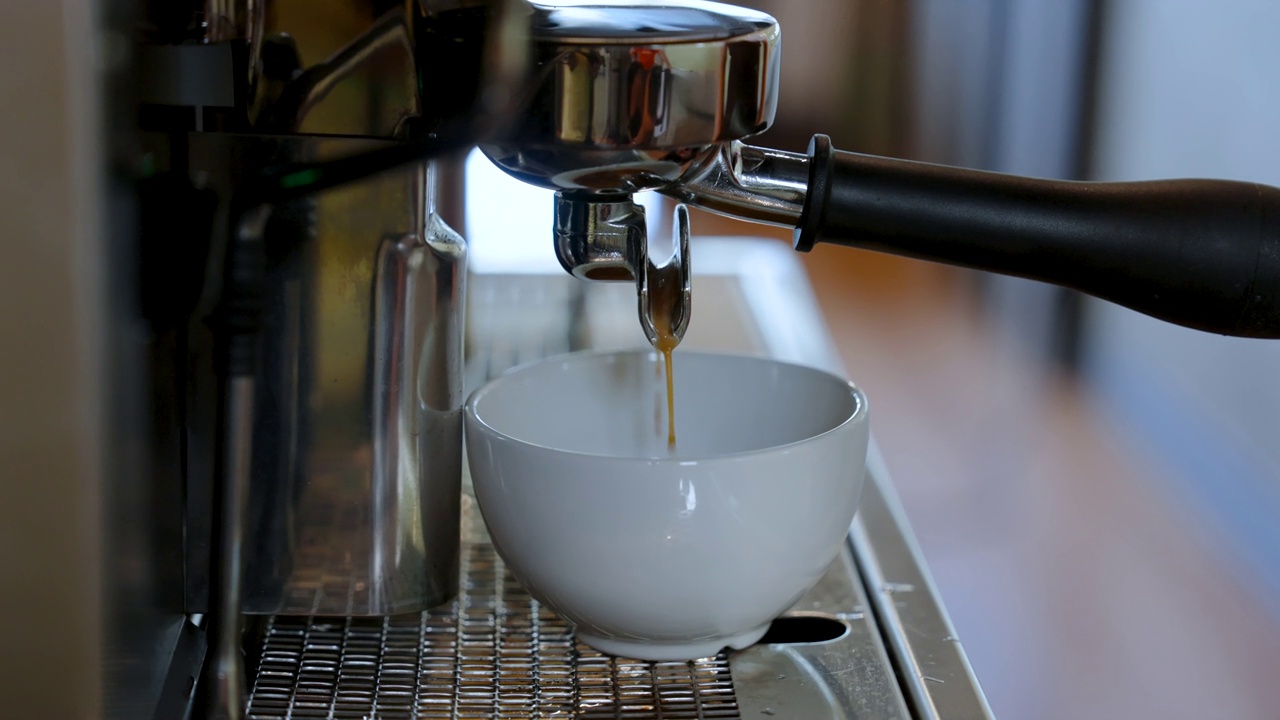 4K，近距离咖啡杯，一侧有把手，适合热咖啡，将咖啡放在插入咖啡机的咖啡把手中，流入等待的咖啡杯。视频素材