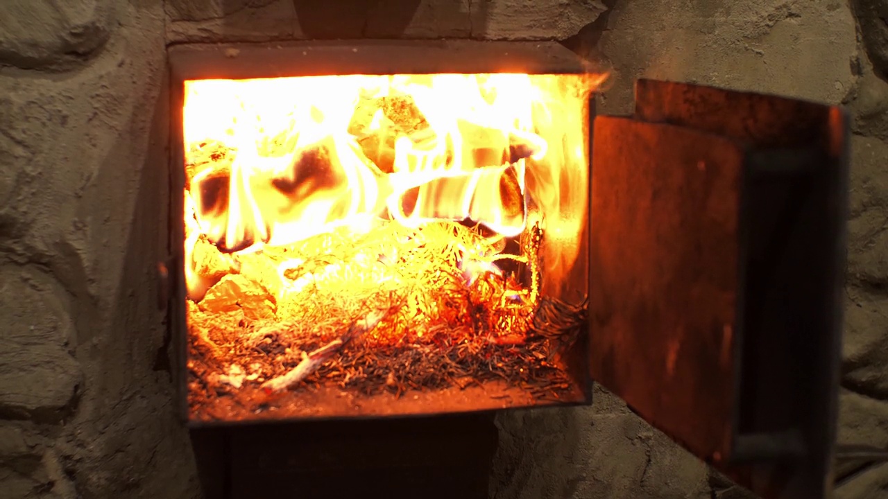 木柴在敞开的炉子里燃烧。一个男人在炉子里生了火来温暖房子。火焰在干燥的木头上燃烧，在壁炉周围营造出舒适的氛围。视频素材
