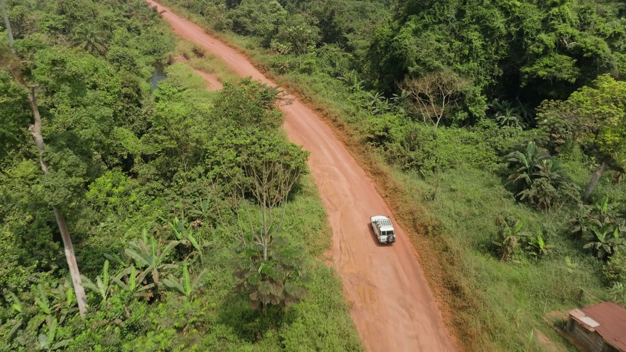 在非洲中部的热带雨林，一辆汽车在伐木路上经过一个小村庄的鸟瞰图视频素材