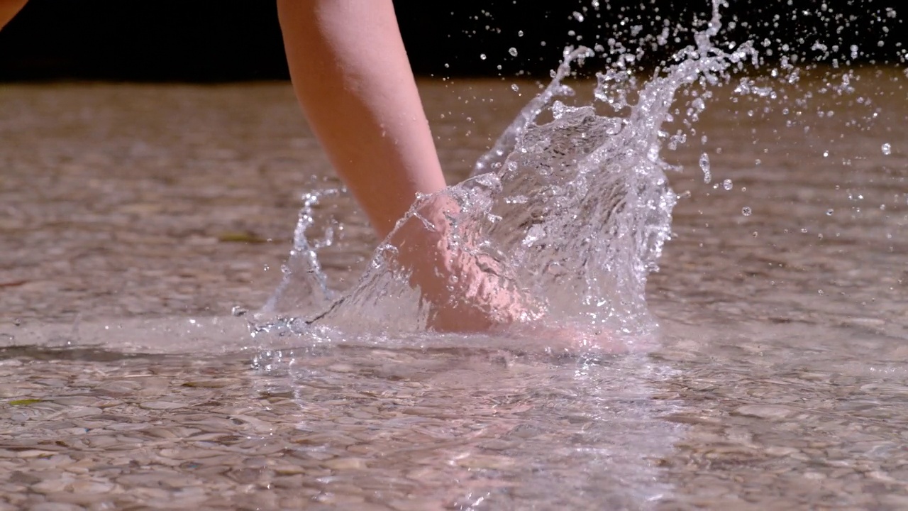 慢镜头，特写:当女人穿过浅浅的高山河流时，水花飞溅视频下载