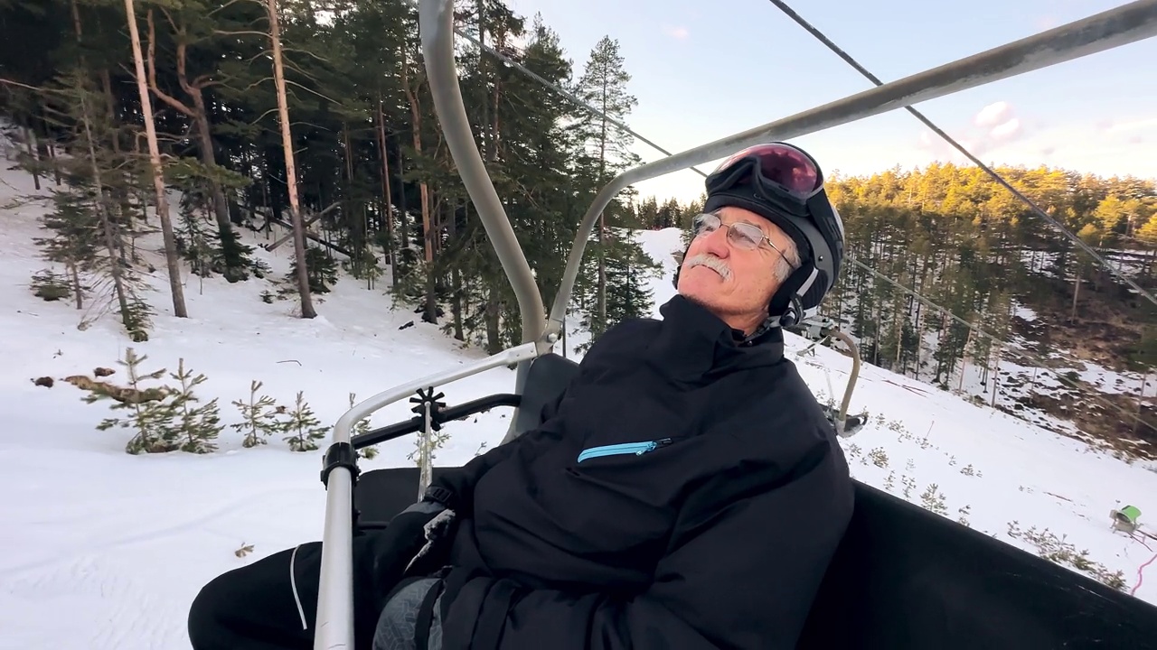 年长的男子，穿着滑雪服坐在滑雪缆车上，享受着新鲜的空气视频下载