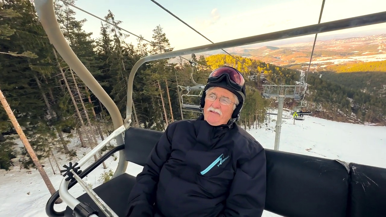 在冬天，穿着滑雪服的老人坐在滑雪缆车上欣赏大自然的景色视频下载