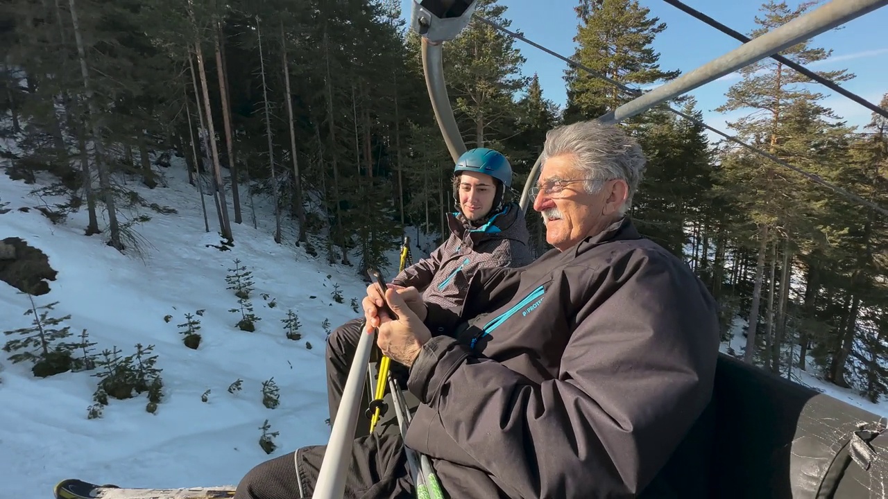 白人老人在一起乘坐滑雪缆车时，向他的孙子展示手机上的东西视频下载