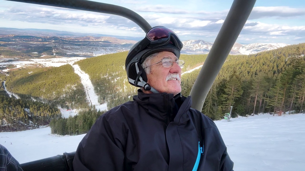 在冬天，穿着滑雪服的老人在滑雪缆车上欣赏大自然的景色视频下载