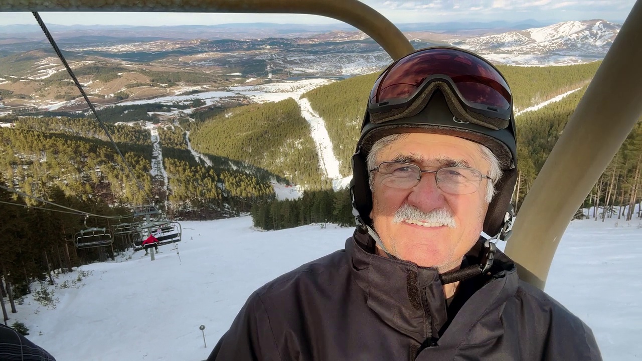 白人老年男子的肖像，穿着滑雪服骑在滑雪缆车上视频下载