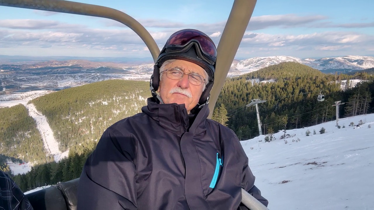 在冬天，穿着滑雪服的老人在滑雪缆车上欣赏大自然的景色视频下载