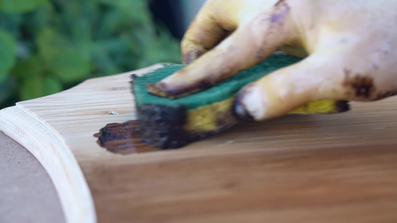 戴手套的木工在车间用保护性油棕漆对木板表面进行染色，专业木匠用专用工具和液体溶液修复古董风化木家具，以改善和保护其不受破坏视频下载