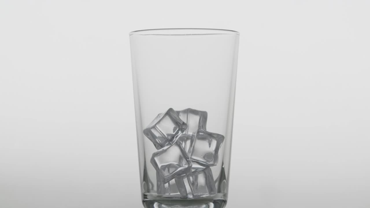 倒透明的碳酸饮料。玻璃杯里装满了冰水，白色背景上有冰块视频素材