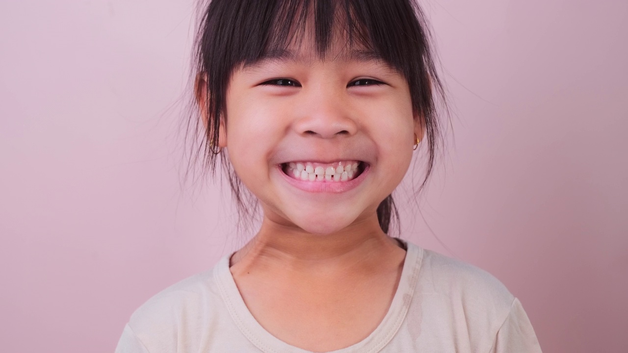 快乐微笑的女孩的肖像孤立在粉红色的背景在工作室。有趣的小女孩在家里看着相机微笑。快乐童年的概念视频素材