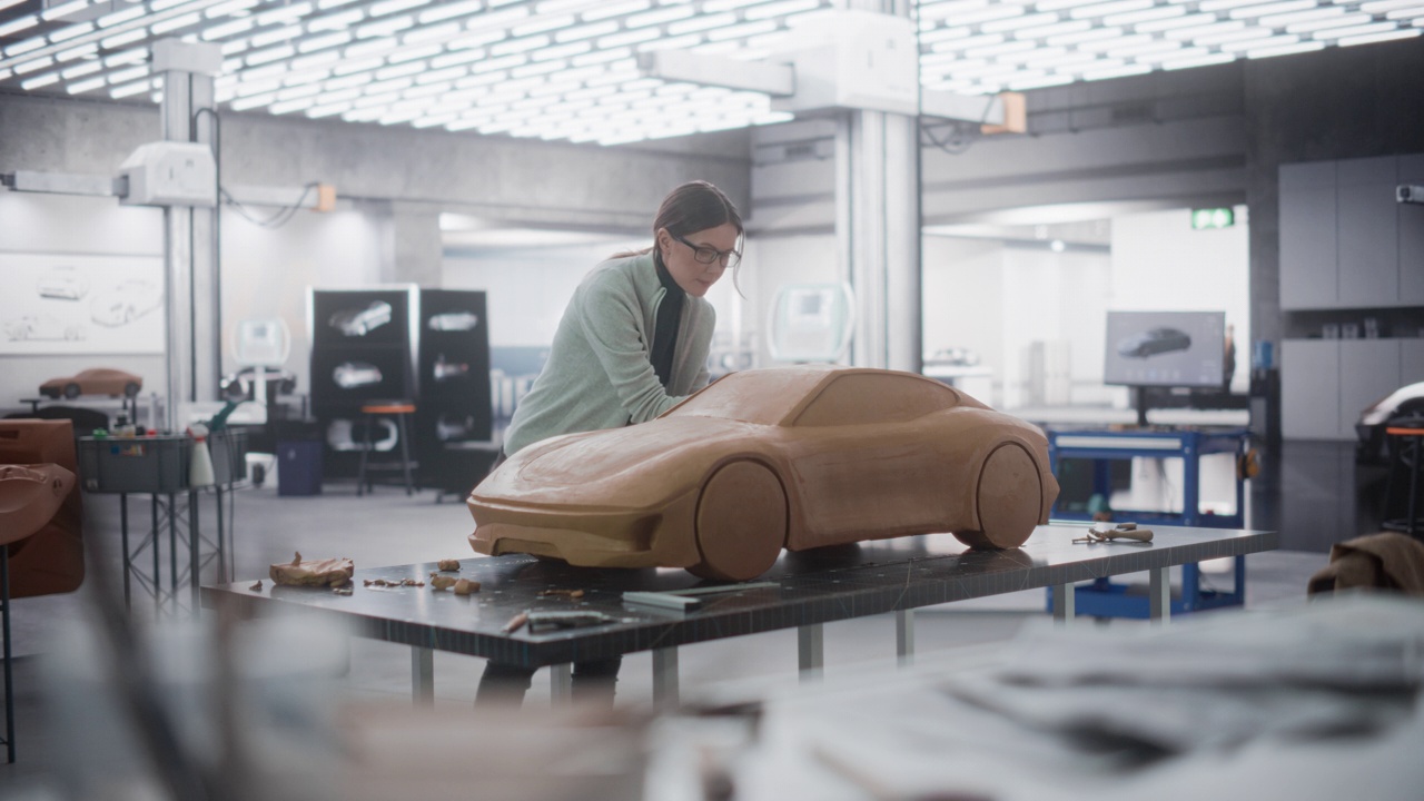 女性汽车设计师使用抹刀创建一个原型车的聚合物建模粘土。在汽车生产厂的研发工作室工作的专注建模师视频素材