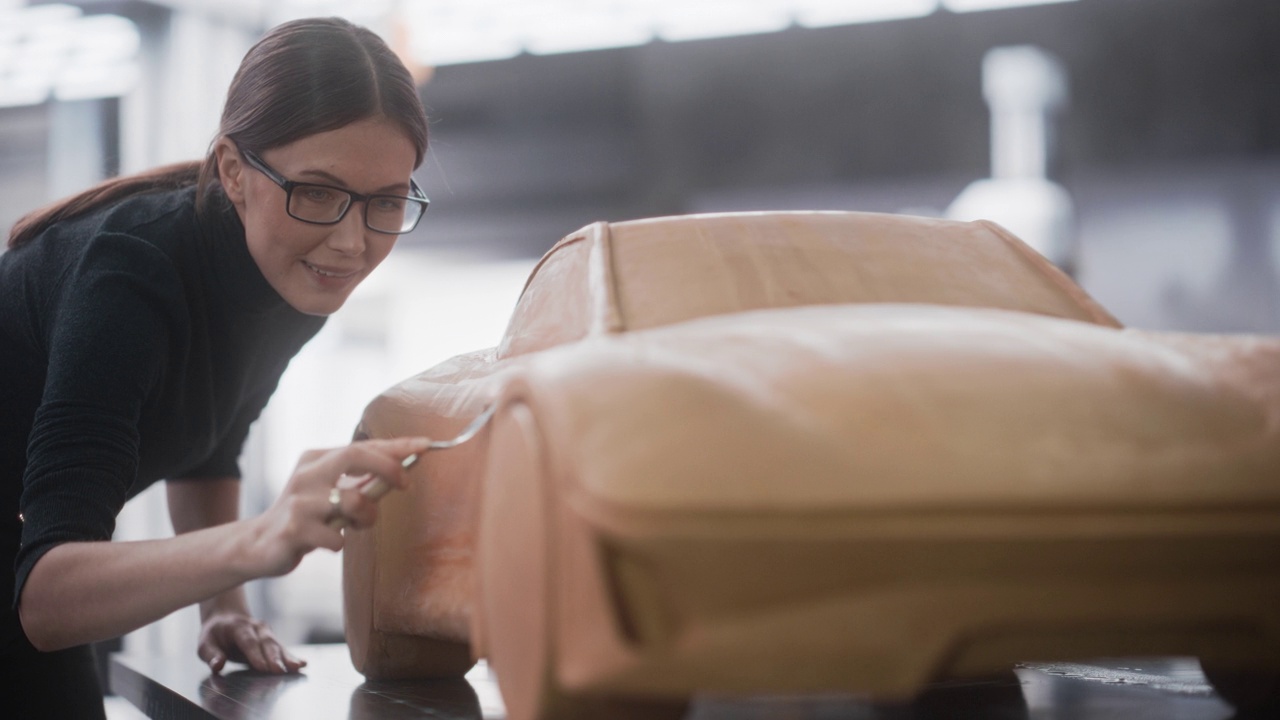 一个年轻的汽车艺术家在她最新的概念车创作上做最后的笔画。女设计师工作在一个原型，雕刻的运动跑车的工业橡皮泥粘土3D模型视频素材