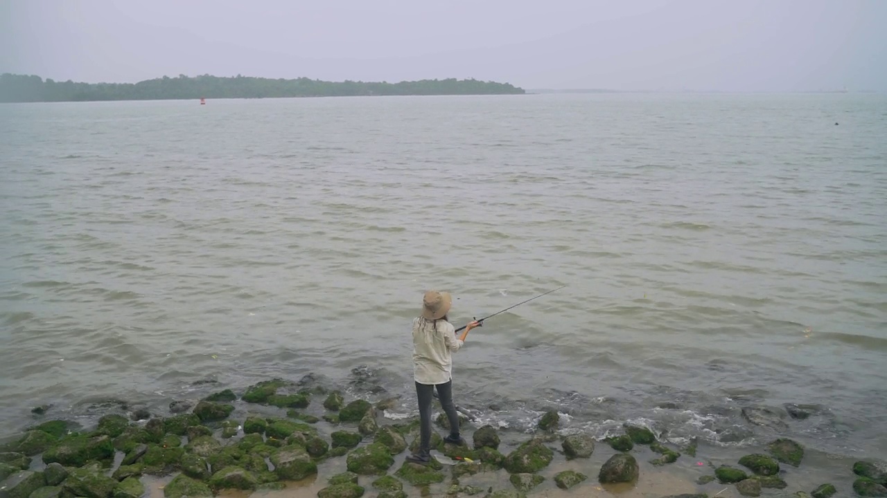 一名亚裔中国妇女站在海边的海滩岩石上钓鱼视频下载