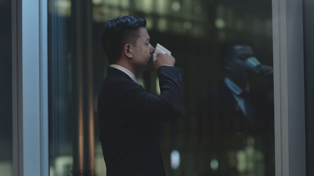 亚洲商人晚上站在窗边喝咖啡视频素材