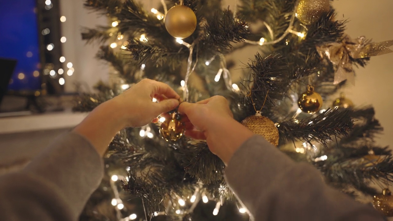 美丽微笑的女人用灯泡装饰家里的圣诞树。在室内布置节日气氛，庆祝圣诞节和新年快乐视频素材