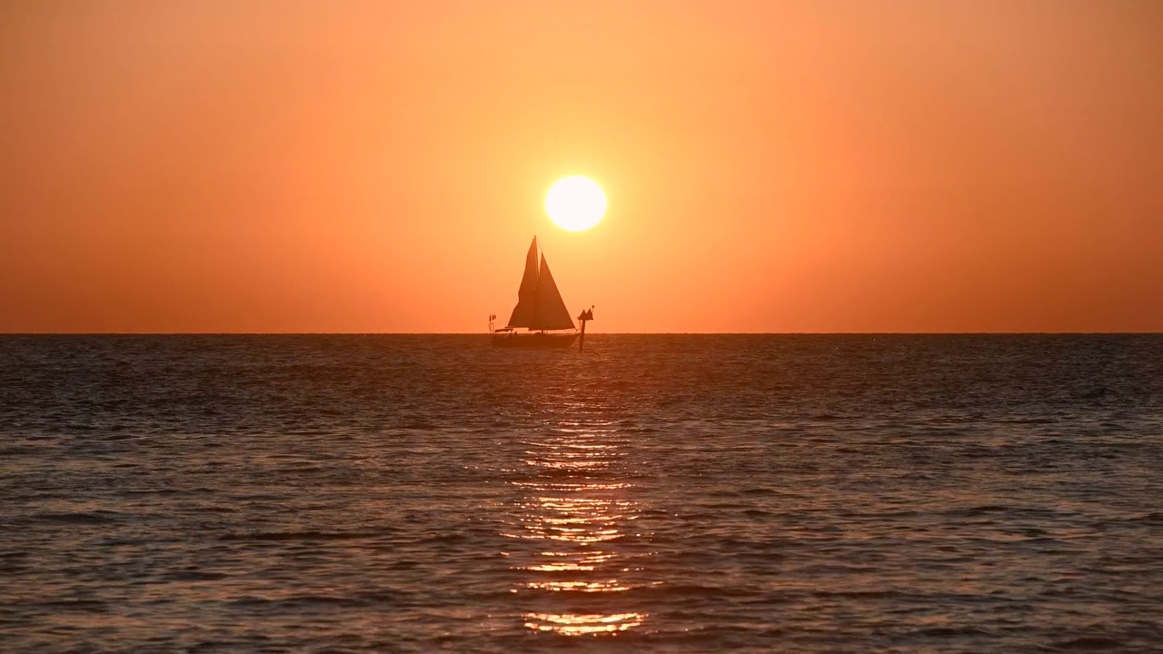 驶向日落——在一个秋天的傍晚，一艘小帆船在夕阳和橙色的天空前航行。美国佛罗里达州清水镇。视频下载