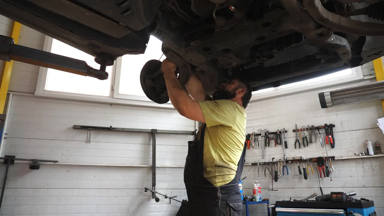 汽车维修厂的机械师用扳手修理汽车。穿着制服的专业修理工在车库的起重车辆下面工作。有人在拧紧螺栓。汽车维修概念视频下载