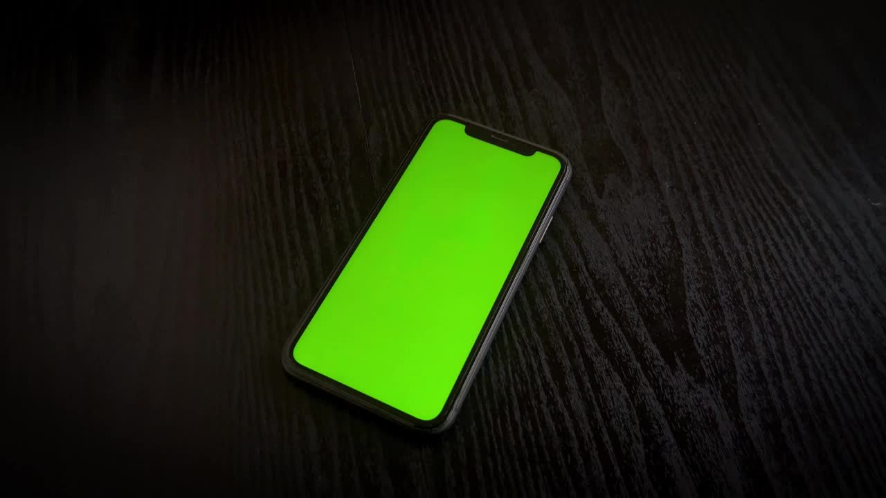 手机，绿屏，手机，手机的绿屏，带绿屏的手机，黑桌子上的智能手机，使用中的技术特写视频素材