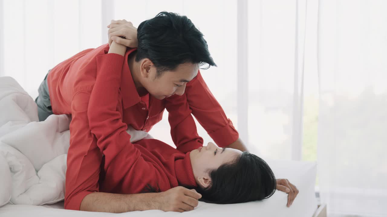 快乐的亚洲情侣躺在床上微笑，一起放松。深情的男人和女人在房子里拥抱在一起。视频素材