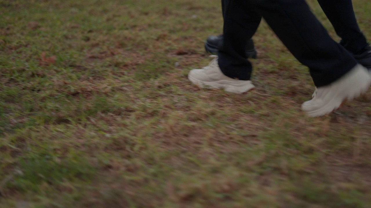 双腿和运动鞋在草地上同步行走。低角度视图视频素材